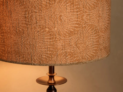 Close-up of the illuminated Winslow Table Lamp's textured orange-tan fabric shade with a subtle pattern, and dark bronze metal base.