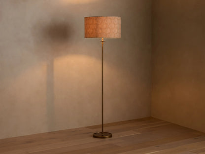 Full view of the Winslow Floor Lamp with antique brass finish and a textured light brown fabric shade, illuminating a room corner.