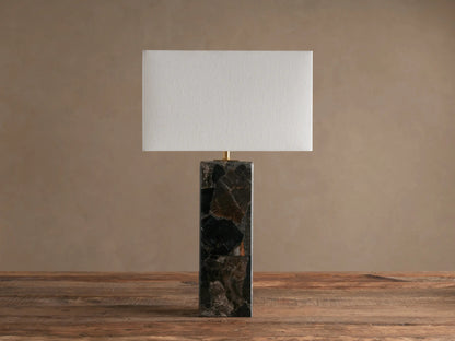 Oren Table Lamp with rectangular white linen shade on a tall dark stone base, standing on a rustic wooden table.