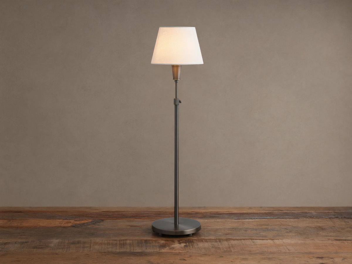 Upright pewter Candice Table Lamp with a creamy white conical shade, standing on a distressed wooden table against a warm neutral wall.