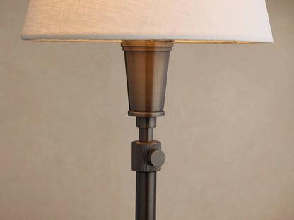 Candice Table Lamp in Pewter with a white conical shade, standing on a rustic wooden table against a brown wall.