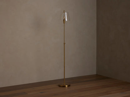Candice Floor Lamp with a brass finish and a clear bell-shaped glass shade, emitting warm light in a dimly lit room.