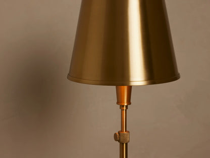 Candice Floor Lamp, brass finish, with a matching brass conical shade, standing upright in a room corner with wood floor.