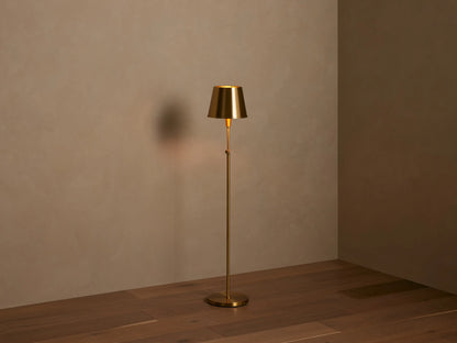 Partial view of Candice Floor Lamp; metallic brass conical shade and stem with a knurled switch, casting a warm glow.