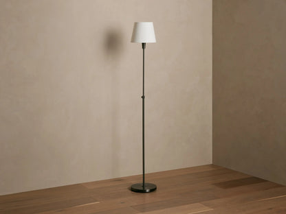Candice Floor Lamp with dark pewter stand, white tapered shade emitting warm light, against a beige wall and wood floor.