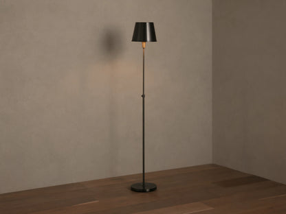 Candice Floor Lamp with a slender dark pewter-finished stand & tapered shade, illuminated, in a room corner with wood floor.
