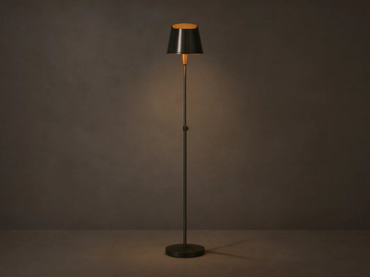 Candice Floor Lamp with a slender dark pewter-finished stand & tapered shade, illuminated, in a room corner with wood floor.