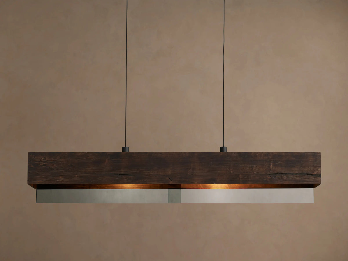Lena Linear Chandelier: a dark alder wood beam with ochre finish and mirrored glass bottom, emitting warm light, suspended by two black cords.
