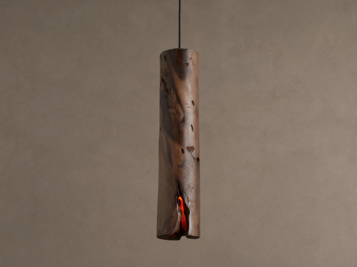 Dedalo Pendant, a cylindrical milpa wood light with natural texture, hangs vertically. An orange glow emanates from a front crack.