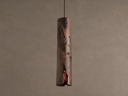 Dedalo Pendant, a cylindrical milpa wood light with natural texture, hangs vertically. An orange glow emanates from a front crack.