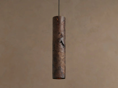 Dedalo Pendant, a cylindrical milpa wood light with natural texture, hangs vertically. An orange glow emanates from a front crack.