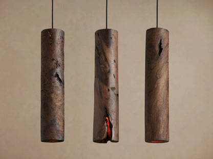 Dedalo Pendant, a dark milpa wood cylinder with a natural, deep vertical crack glowing warm orange from within, against a light wall.