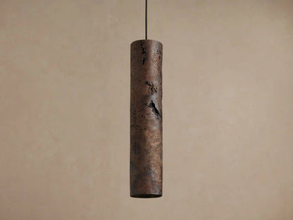 Three cylindrical Dedalo Pendants of dark milpa wood hang, natural cracks emitting warm orange light against a light wall.