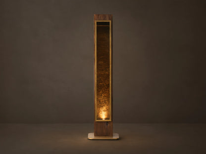 Vigas Floor Lamp: Tall wooden lamp with brass trim, illuminated mirrored glass revealing a textured interior, standing on wood floor.