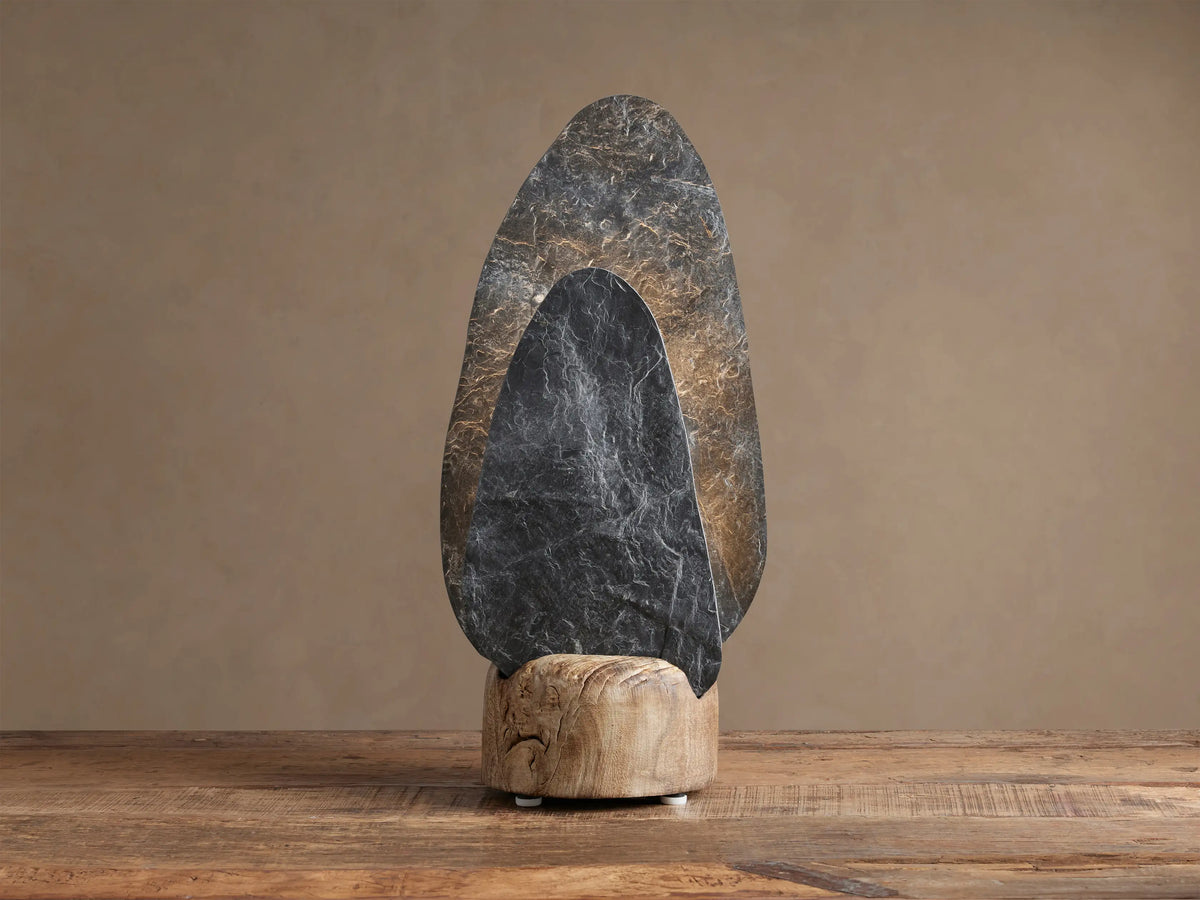 Shinto Table Lamp. Two irregular slate stone shades, dark gray front, lighter illuminated rear, in a natural wood base on a wood table.