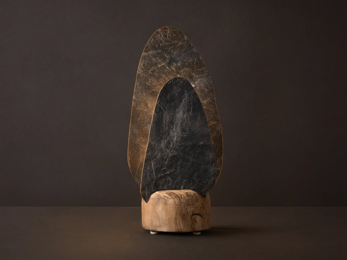 Shinto Table Lamp. Two irregular slate stone shades, dark gray front, lighter illuminated rear, in a natural wood base on a wood table.
