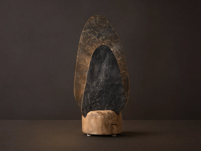 Shinto Table Lamp. Two irregular slate stone shades, dark gray front, lighter illuminated rear, in a natural wood base on a wood table.