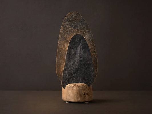 Shinto Table Lamp. Two irregular slate stone shades, dark gray front, lighter illuminated rear, in a natural wood base on a wood table.