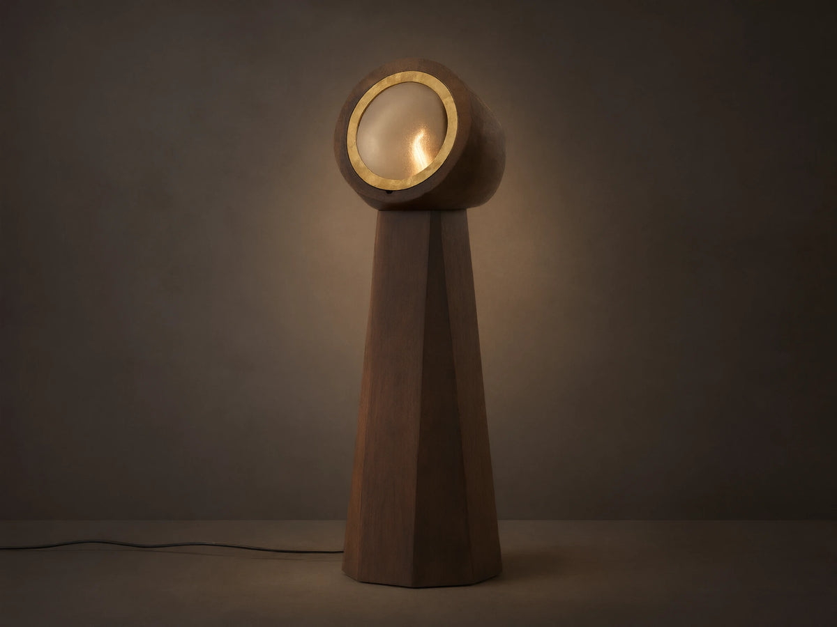 Agustin Floor Lamp: Dark wood faceted base with a round, gold-rimmed opaque glass light fixture, glowing warmly.