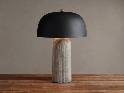 Ira Striped Table Lamp with black dome shade, light-colored vertically ribbed base, on wood table, softly lit.