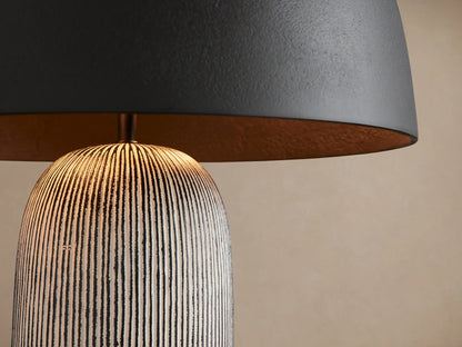 Ira Striped Table Lamp with black dome shade, textured gray striped cylindrical base, and small gold knob, on wooden table.