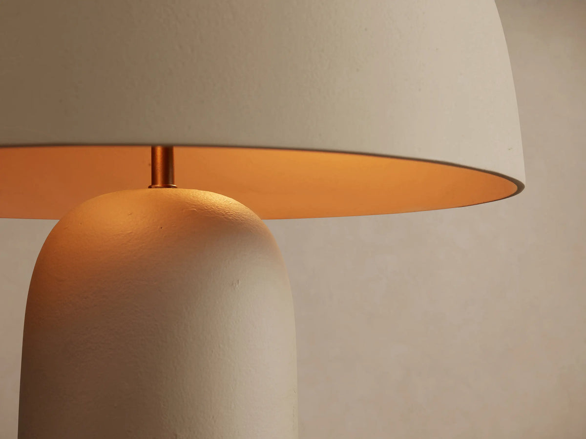 Ira Table Lamp: matte gray mushroom-shaped lamp with a cylindrical base and small gold top accent, on a wooden table.