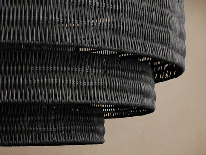 Black Paloma Chandelier with three tiered, handwoven rattan shades, hanging from a dark chain against a beige wall.