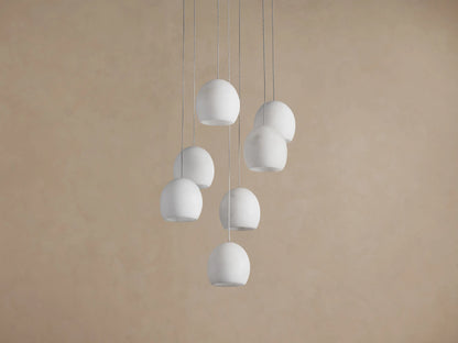 Arica Round Chandelier with multiple white spherical alabaster shades hanging from thin cables against a beige wall.