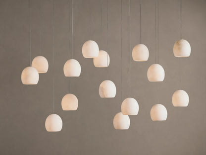 Arica Linear Chandelier with multiple glowing, spherical alabaster shades hanging at varying heights against a warm neutral wall.