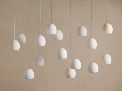 Arica Linear Chandelier with multiple glowing, spherical alabaster shades hanging at varying heights against a warm neutral wall.