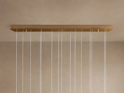 Multiple spherical, translucent alabaster shades of the Arica Linear Chandelier glow softly, suspended by thin silver cables.