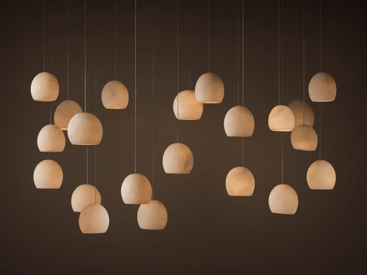 Arica Linear Chandelier with multiple glowing, spherical alabaster shades hanging at varying heights against a warm neutral wall.