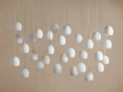 Arica Linear Chandelier with numerous natural alabaster curved shades, glowing softly, hanging from thin cables at various lengths.