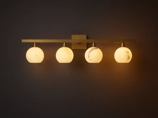 Arica Wall Sconce with four illuminated round glass shades mounted on a horizontal brass fixture above a mirror.