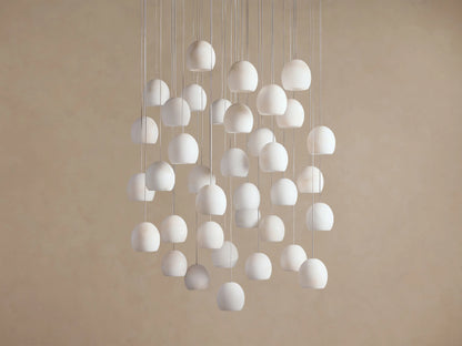 Arica Round Chandelier with numerous white, round alabaster shades suspended at varying heights against a light beige wall.