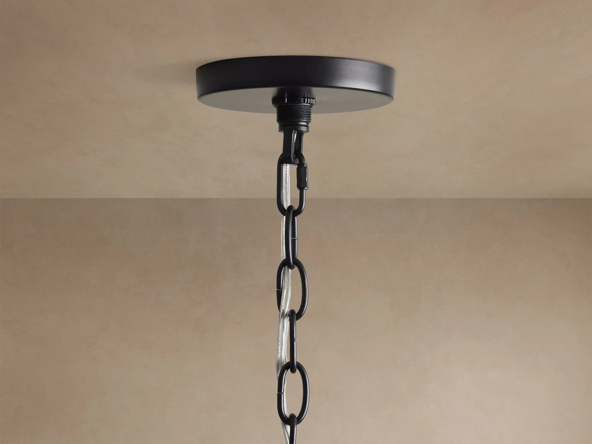 Close-up of Rosalind Rattan Chandelier in Black. Matte black iron frame, a rattan-wrapped arm, and a lit candelabra bulb.