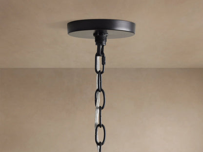 Close-up of Rosalind Rattan Chandelier in Black. Matte black iron frame, a rattan-wrapped arm, and a lit candelabra bulb.
