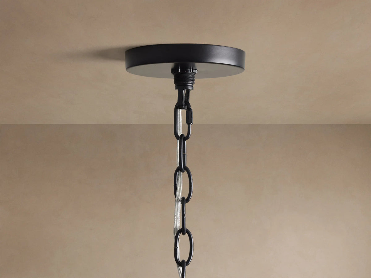 Close-up of Rosalind Chandelier's matte black iron frame with curved details and two lit candelabra bulbs against a beige wall.