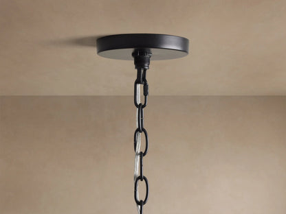 Close-up of Rosalind Chandelier's matte black iron frame with curved details and two lit candelabra bulbs against a beige wall.