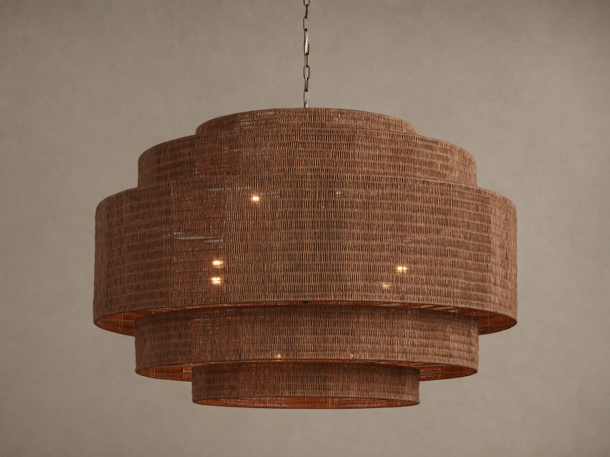 Paloma 52" tiered brown woven rattan chandelier hangs from a chain, with warm light glowing from within its shades.