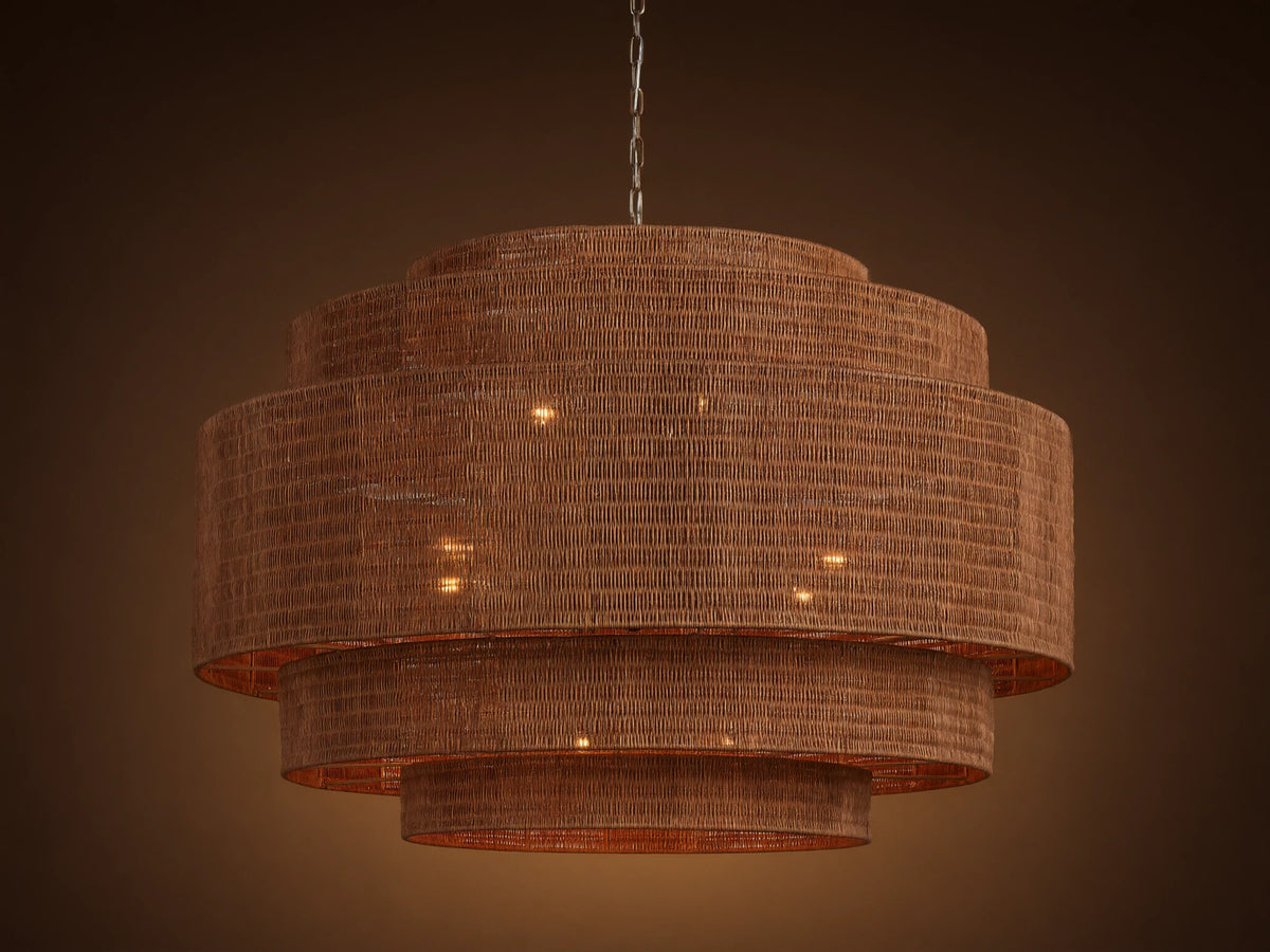 Paloma 52" tiered brown woven rattan chandelier hangs from a chain, with warm light glowing from within its shades.