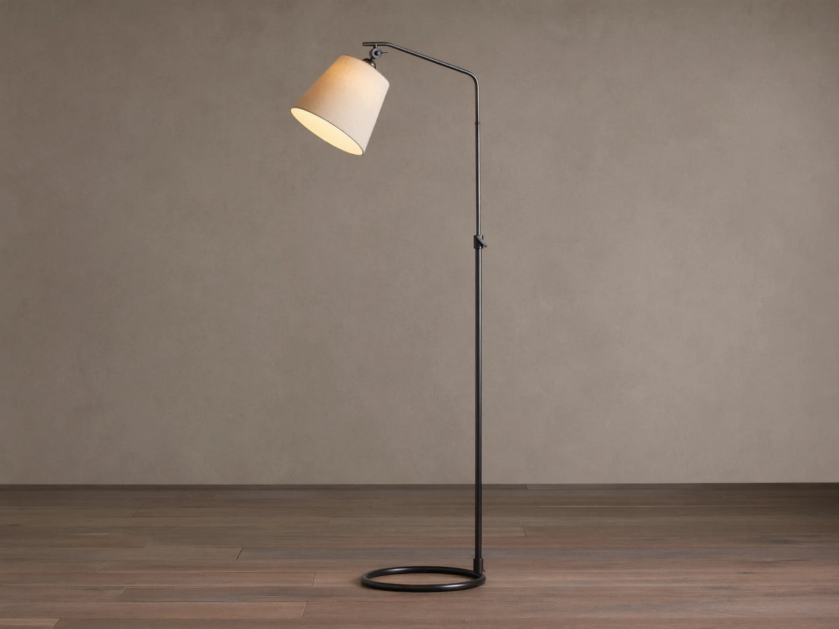 Kellen Floor Lamp: oil-rubbed bronze adjustable stand, angled beige linen shade, lit, on wood floor against plain wall.