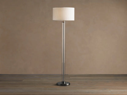 Tall Glass Column Floor Lamp with a clear glass stem, round black iron base, and a cream linen drum shade, on a wood floor.