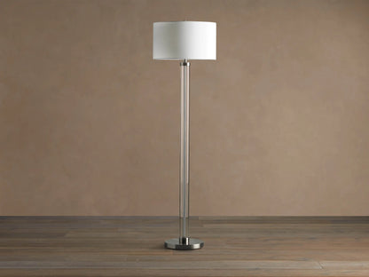 Tall Glass Column Floor Lamp with a clear glass stem, round black iron base, and a cream linen drum shade, on a wood floor.