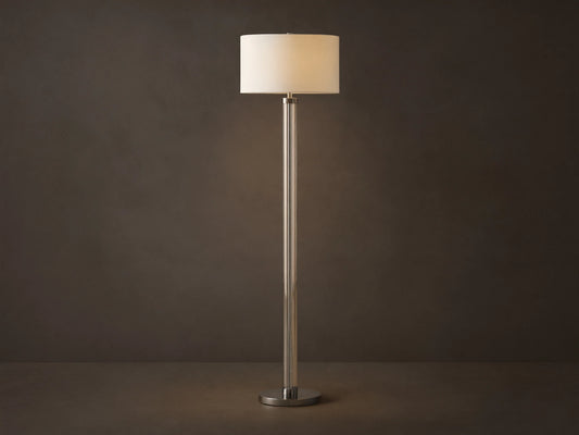 Tall Glass Column Floor Lamp with a clear glass stem, round black iron base, and a cream linen drum shade, on a wood floor.