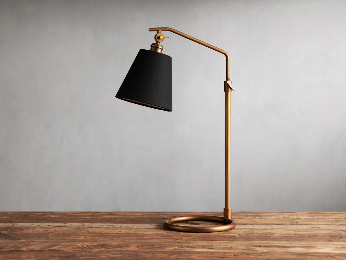 Kellen Antiqued Brass Table Lamp with dark tapered linen shade on adjustable brass stand, placed on wooden surface.