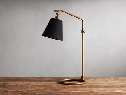 Kellen Antiqued Brass Table Lamp with dark tapered linen shade on adjustable brass stand, placed on wooden surface.