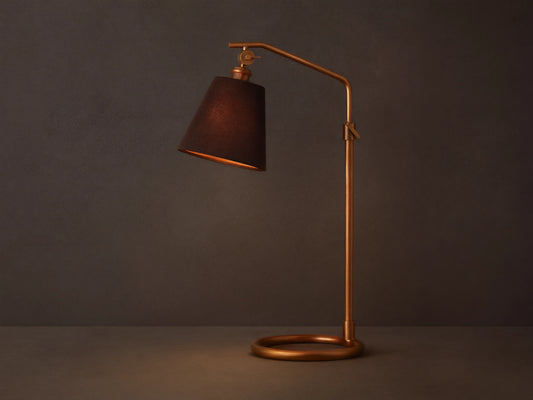 Kellen Antiqued Brass Table Lamp with dark tapered linen shade on adjustable brass stand, placed on wooden surface.