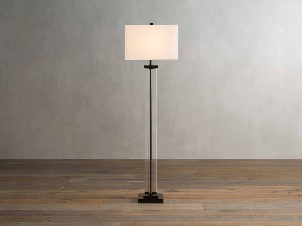 Dawson Floor Lamp with a rectangular white shade, clear crystal and iron base, on a wooden floor against a light wall.