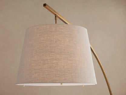 Tadeo Floor Lamp: arched brass-finish iron stand, white marble base, light beige linen drum shade, on a wooden floor.